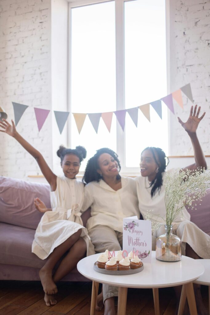 Parcerias e associações A joyful family celebrating Mother's Day with cupcakes and decorations indoors.