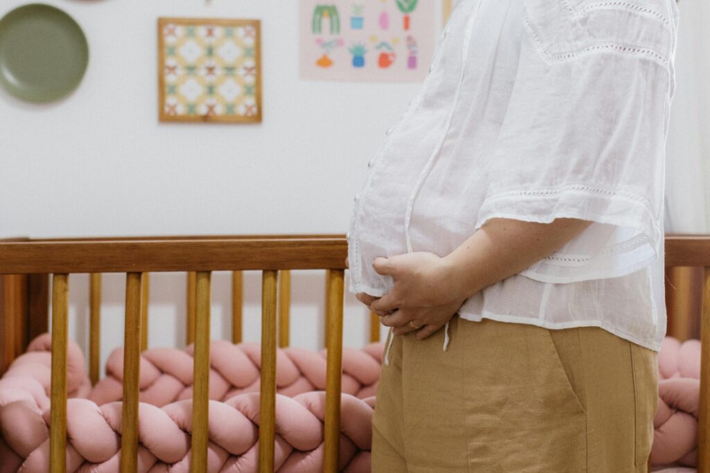 A pregnant woman standing beside a crib in a cozy nursery room.