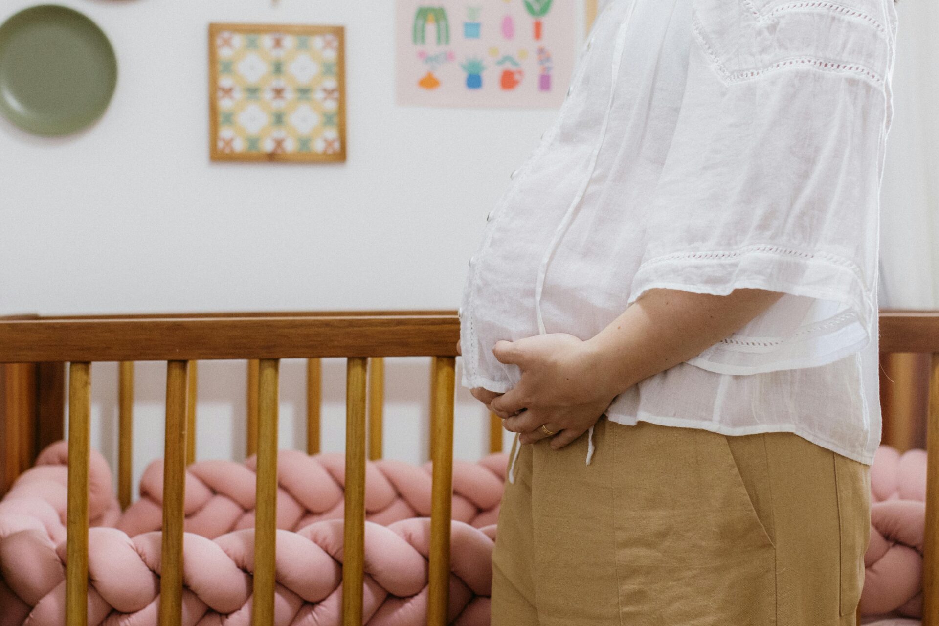 A pregnant woman standing beside a crib in a cozy nursery room.