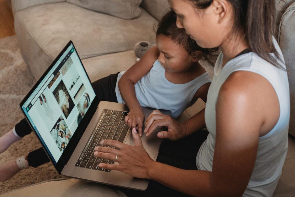 Woman with child sitting on sofa and browsing internet on netbook in living room at home