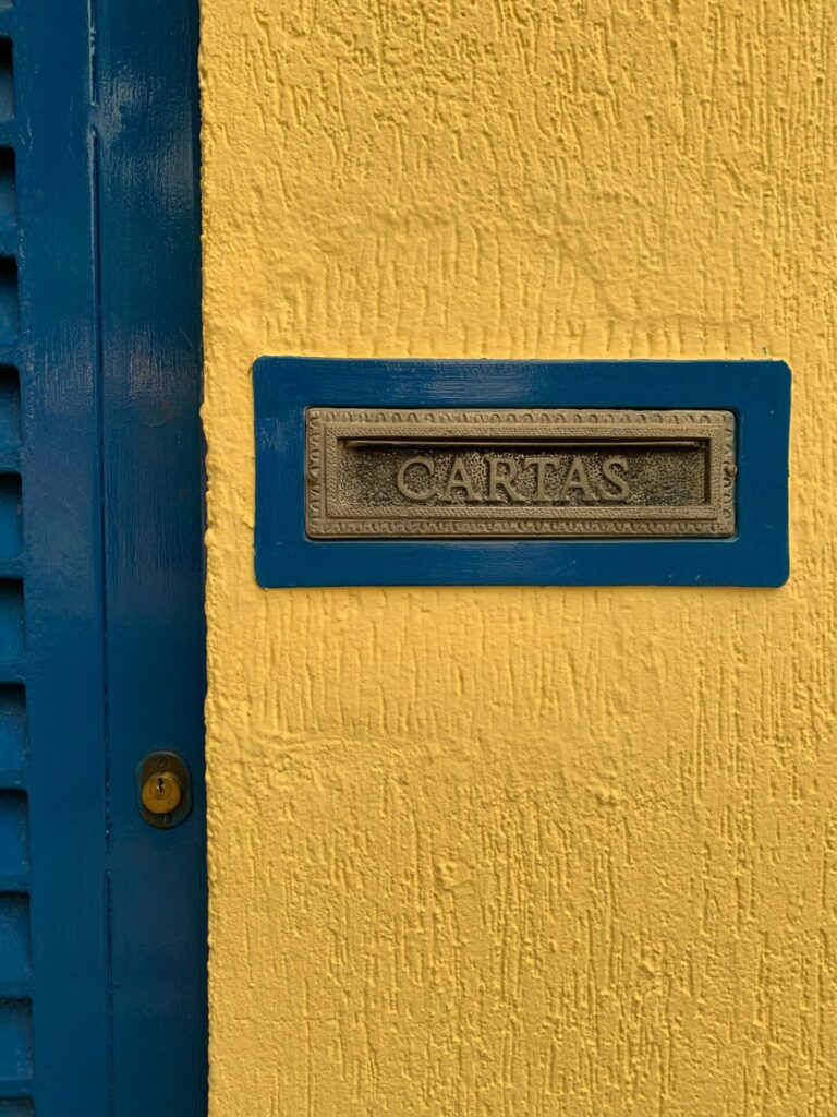 Blue mail slot labeled 'Cartas' on a textured yellow wall offering striking contrast.