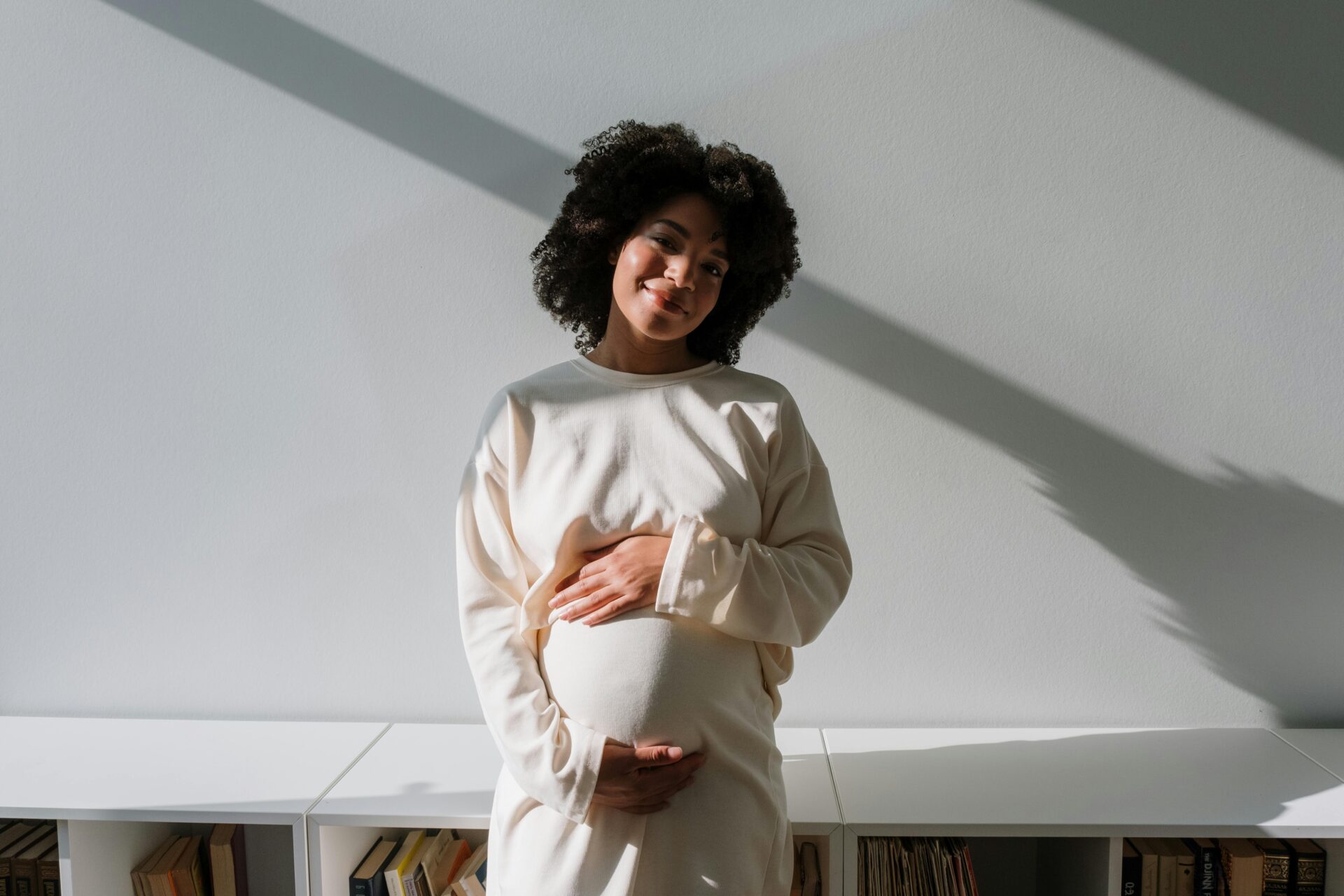 Beautiful pregnant woman with curly hair embracing maternity in a serene indoor setting.