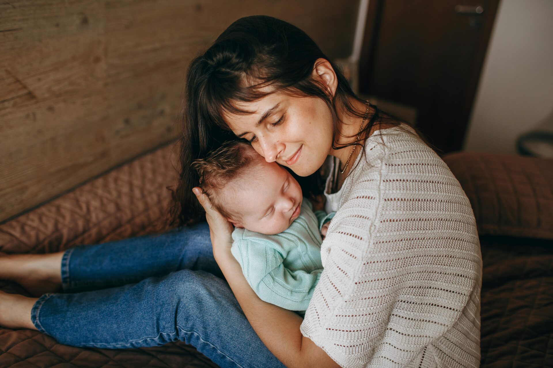 A tender moment of a mother lovingly embracing her baby indoors, highlighting family warmth.