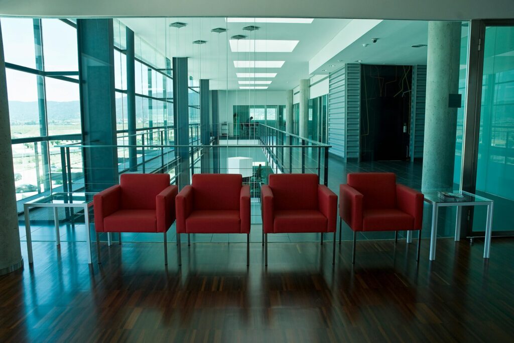 A spacious modern office lobby featuring bright red chairs and glass windows with abundant natural light.