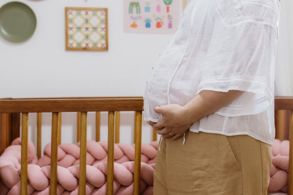 A pregnant woman standing beside a crib in a cozy nursery room.