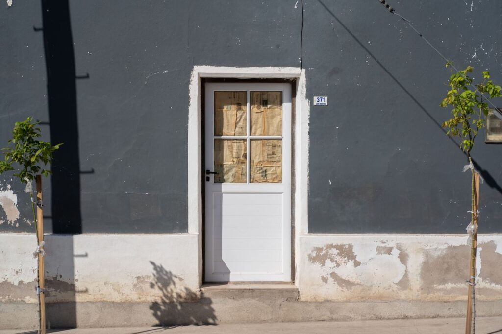 Photograph of a rustic white door on a gray facade in La Cruz, C&oacute;rdoba, Argentina.
