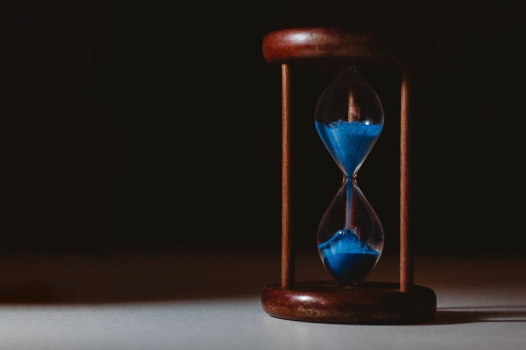 A minimalist close-up of a wooden hourglass with blue sand flowing, symbolizing the passage of time.