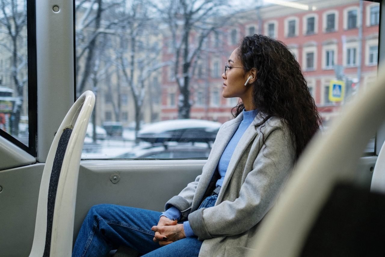 A woman wearing earphones gazes out the window of a bus on a snowy winter day.