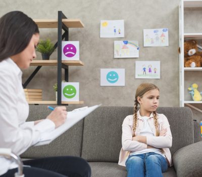 depressed-girl-sitting-sofa-with-female-psychologist-writing-note-clipboard